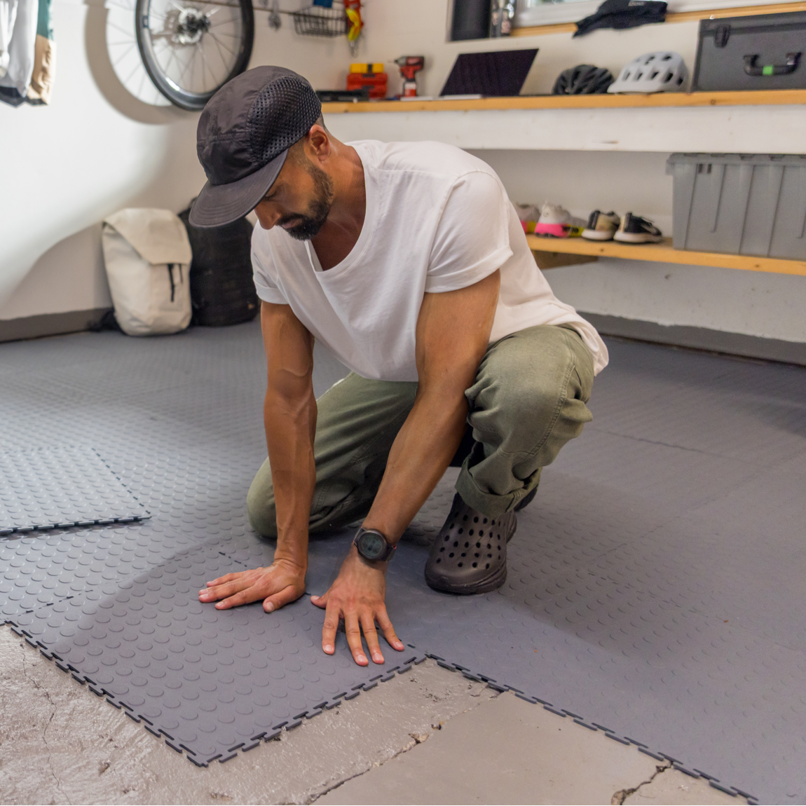 Person installing interlocking tile floor tiles in a garage workshop with bicycles and tools.