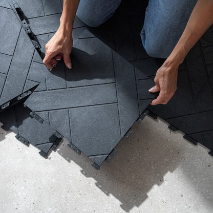 Person installing interlocking black tiles on a concrete surface
